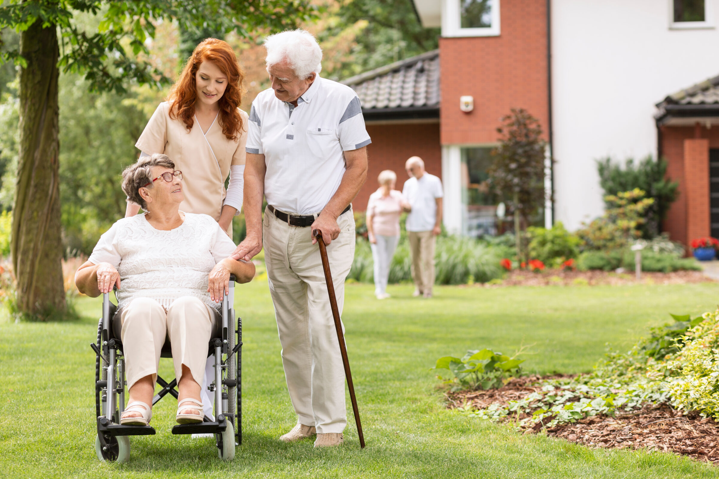 nursing home professional and elderly patrons walking on green grass outside