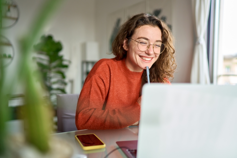 young woman in red shirt on a computer smiling and about to take her gig from freelance to full-time