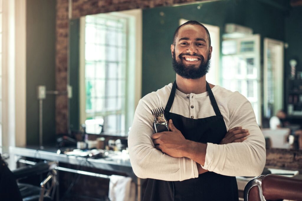 bearded tan entrepreneur man with arms crossed and a hair electric razor in hand smiling